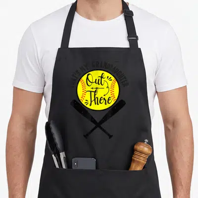 Softball grandma granddaughter aprons - Yellow softball with red stitching, crossed bats, and arched text reading — shown on a black cotton canvas apron against a white background