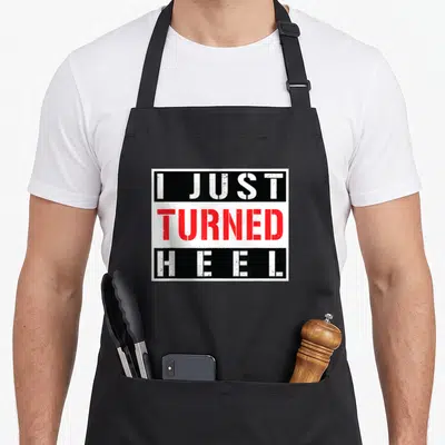 Turned wrestling apron - Stacked white and red text reading I JUST TURNED HEEL inside black rectangular bands — shown on a black cotton canvas apron against a white background