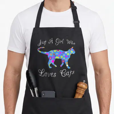 Funny cat kitten apron - Blue cat silhouette filled with white purple yellow flowers surrounded by Just A Girl Who — shown on a black cotton canvas apron against a white background
