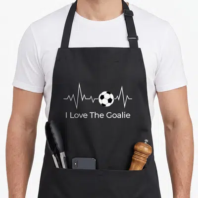 Soccer goalkeeper apron - I Love The Goalie text below a white heartbeat line with a black and white soccer ball — shown on a black cotton canvas apron against a white background
