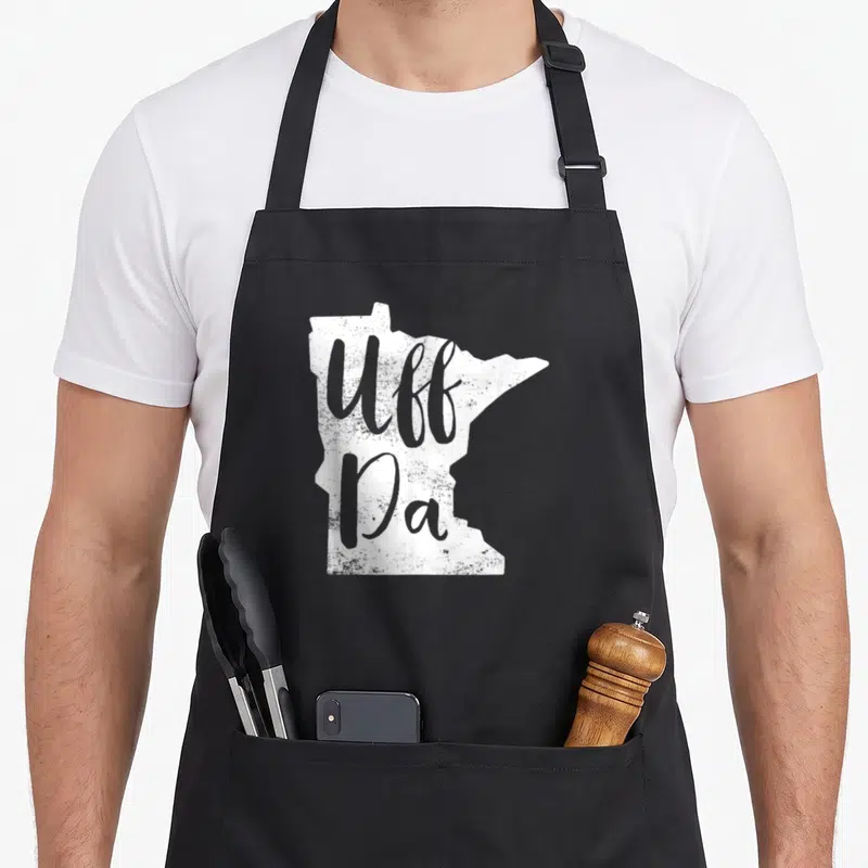 Uff minnesota apron - Distressed white Minnesota map silhouette with grey Uff Da script text — shown on a black cotton canvas apron against a white background