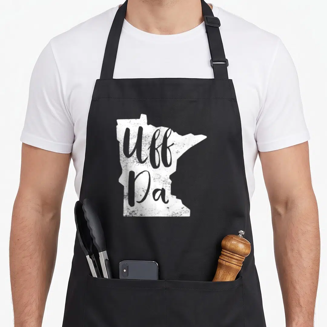 Uff minnesota apron - Distressed white Minnesota map silhouette with grey Uff Da script text — shown on a black cotton canvas apron against a white background