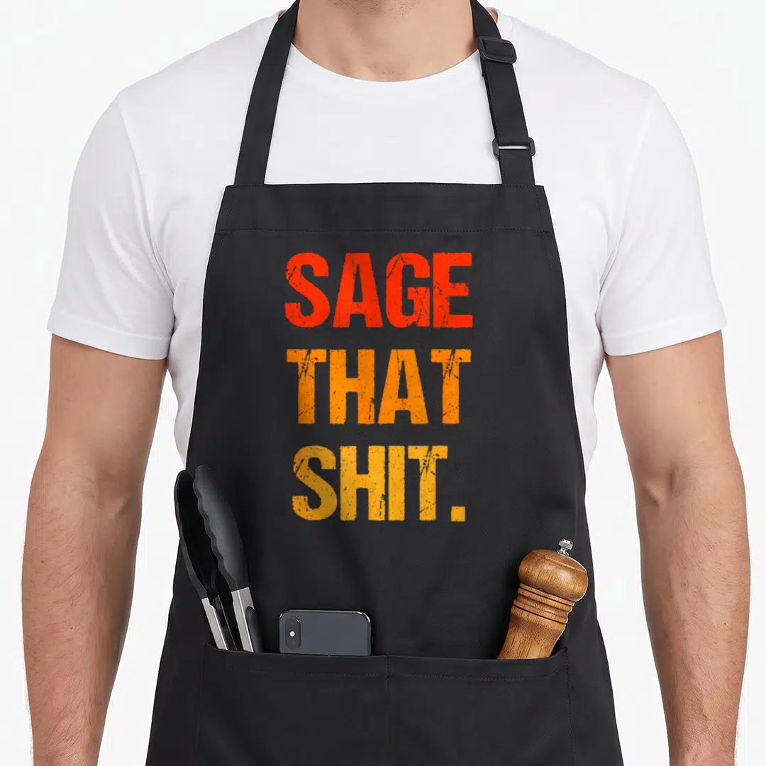 Funny cleansing sage apron - Distressed red and orange text reading SAGE THAT SHIT stacked vertically — shown on a black cotton canvas apron against a white background