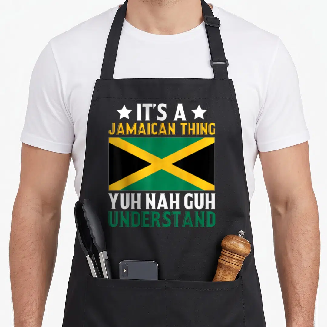 Yuh jamaican american apron - Jamaican flag centered between IT'S A JAMAICAN THING and YUH NAH GUH UNDERSTAND text — shown on a black cotton canvas apron against a white background