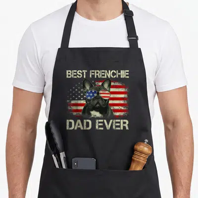Frenchie american flag apron - Best Frenchie Dad Ever text over distressed flag and sunglasses-wearing French Bulldog — shown on a black cotton canvas apron against a white background