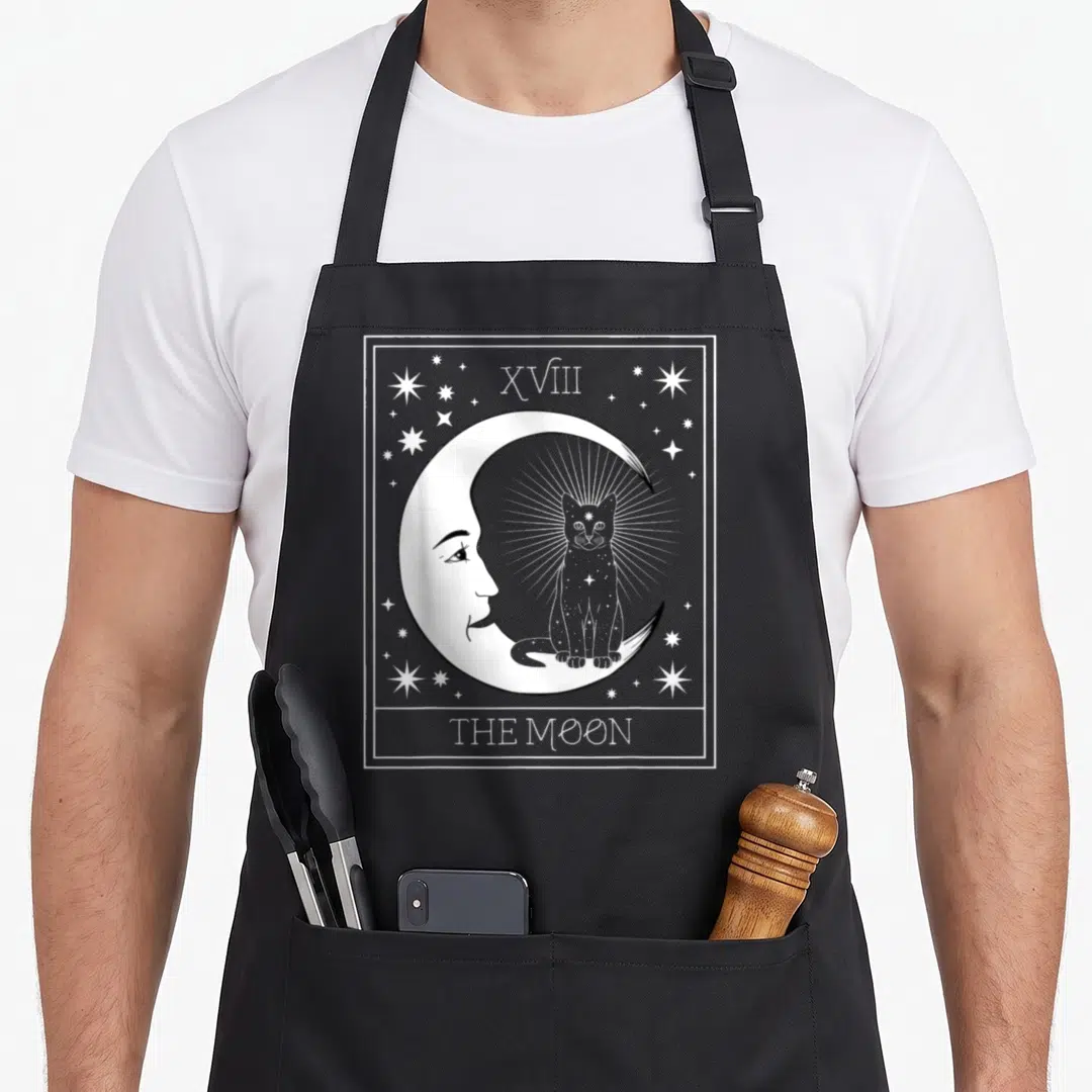 Card cat apron - White line art of crescent moon with face and seated cat inside bordered by stars and text — shown on a black cotton canvas apron against a white background