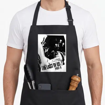 Hand us aprons - Hand holding hammer over dark mirror reflection with distressed text at bottom — shown on a black cotton canvas apron against a white background