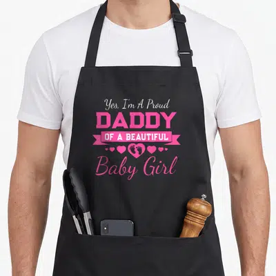 Announcement father day apron - Pink and white Yes I'm A Proud Daddy OF A BEAUTIFUL Baby Girl text with ribbon — shown on a black cotton canvas apron against a white background