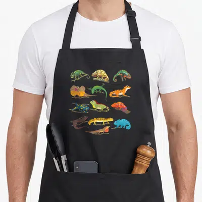 Collage dragon apron - Twelve colorful cartoon lizards perched on brown branches in a grid pattern — shown on a black cotton canvas apron against a white background