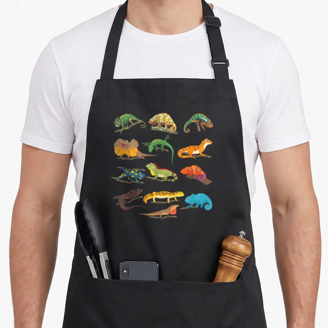 Collage dragon apron - Twelve colorful cartoon lizards perched on brown branches in a grid pattern — shown on a black cotton canvas apron against a white background