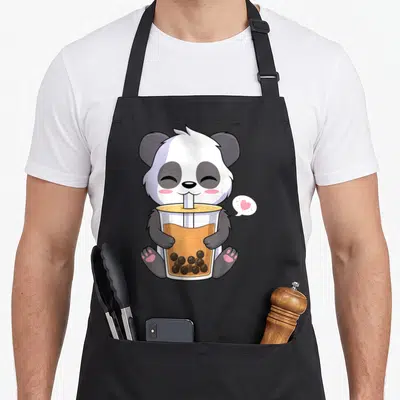 Drinking anime apron - Cartoon panda sitting with bubble tea cup and pink heart speech bubble — shown on a black cotton canvas apron against a white background