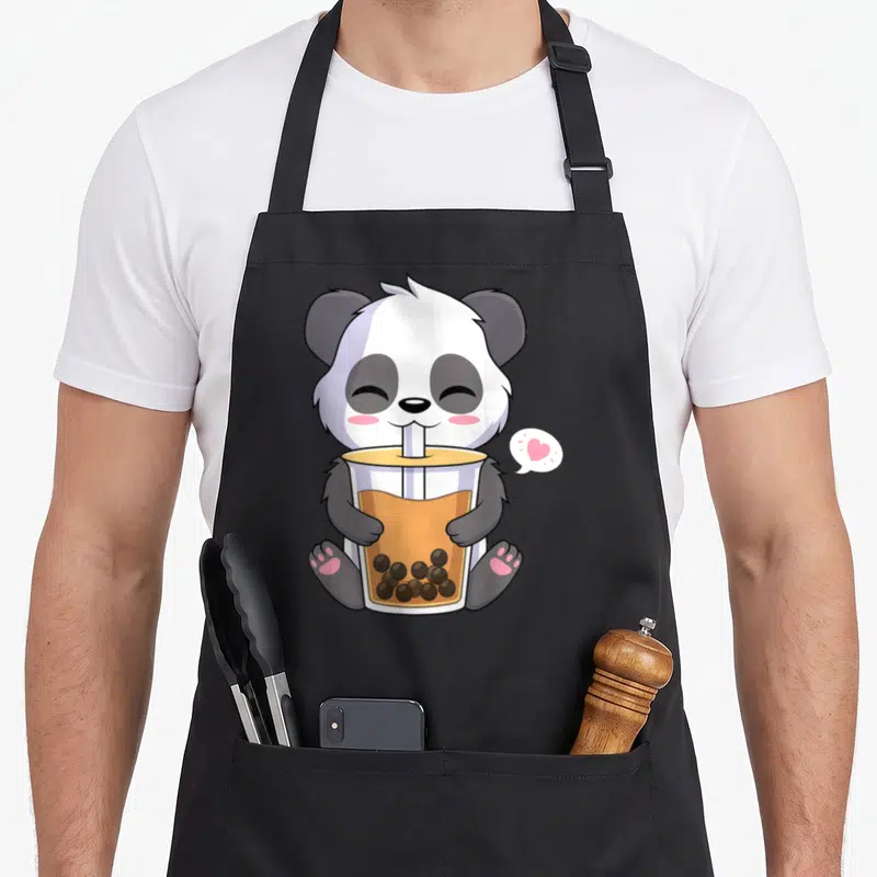 Drinking anime apron - Cartoon panda sitting with bubble tea cup and pink heart speech bubble — shown on a black cotton canvas apron against a white background