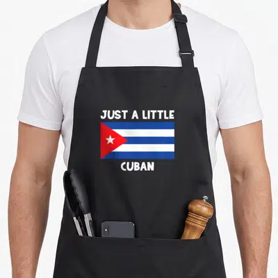 Funny cuban apron - Cuban flag in blue white and red centered between white text reading just a little cuban — shown on a black cotton canvas apron against a white background