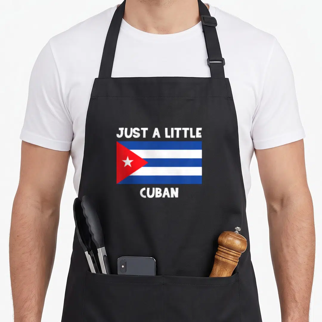 Funny cuban apron - Cuban flag in blue white and red centered between white text reading just a little cuban — shown on a black cotton canvas apron against a white background