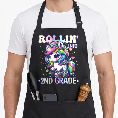 2nd unicorn apron - Cartoon unicorn on roller skates with backpack and scattered stars in rainbow colors — shown on a black cotton canvas apron against a white background