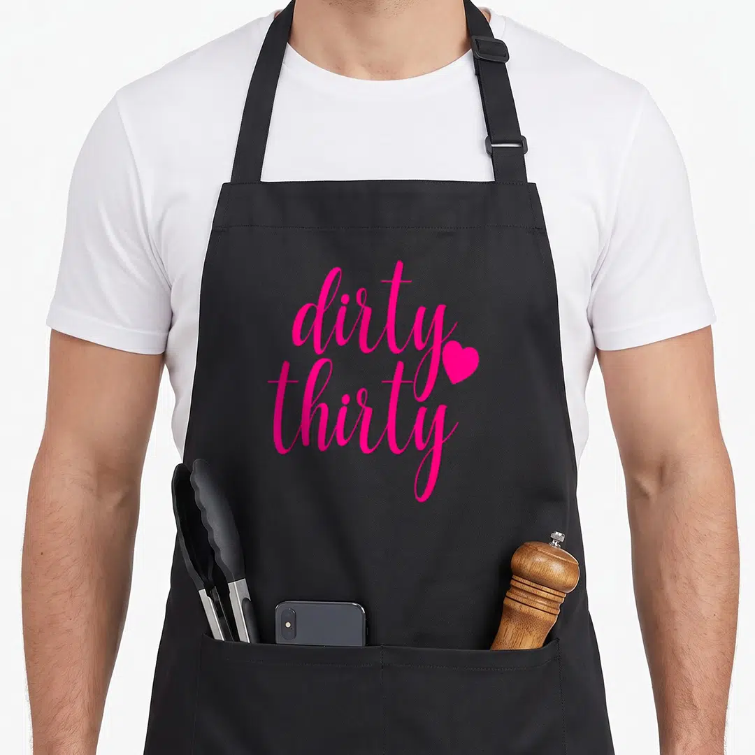 Hot funny dirty aprons - Pink script text reading dirty thirty with a heart icon — shown on a black cotton canvas apron against a white background