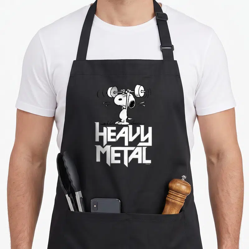 Cute metal heavy apron - Snoopy lifting a barbell with stacked HEAVY METAL text in black and white cartoon style — shown on a black cotton canvas apron against a white background
