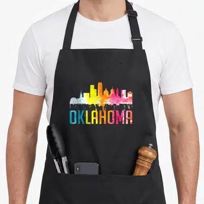 Oklahoma skyline art apron - Colorful watercolor Oklahoma skyline with paint drips and gradient text — shown on a black cotton canvas apron against a white background
