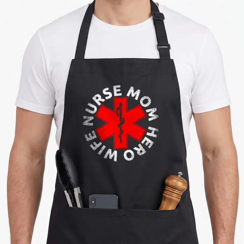 Hero white nurse apron - Red Star of Life with snake and white NURSE MOM HERO WIFE text in distressed circle — shown on a black cotton canvas apron against a white background