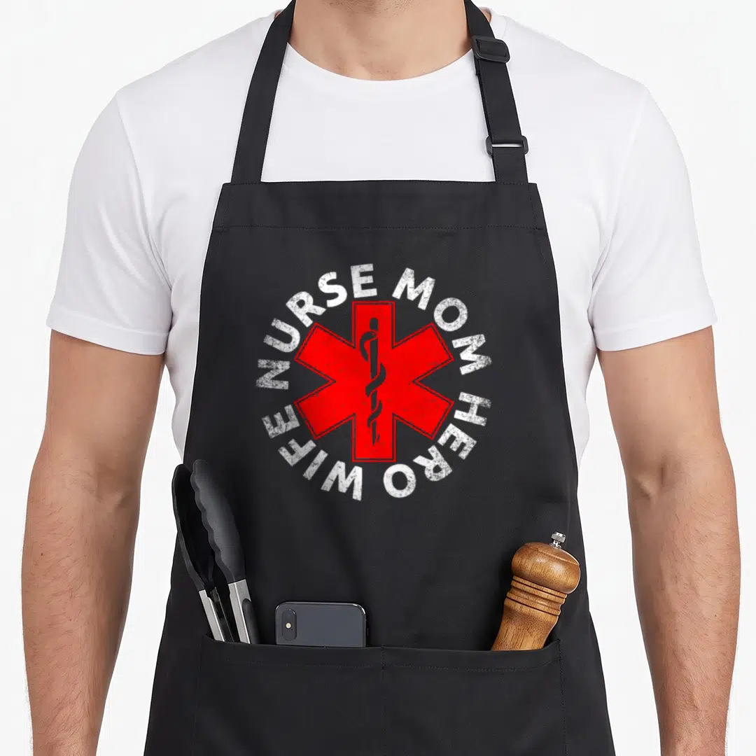 Hero white nurse apron - Red Star of Life with snake and white NURSE MOM HERO WIFE text in distressed circle — shown on a black cotton canvas apron against a white background