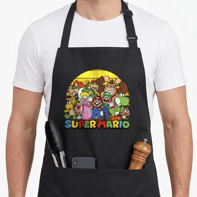 Portrait novelty apron - Super Mario characters clustered before yellow sun with colorful text at bottom — shown on a black cotton canvas apron against a white background