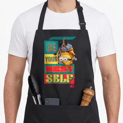 Despicable banana addict apron - Upside down yellow Minion tied in rope over Be Your Best Self text on colored blocks — shown on a black cotton canvas apron against a white background
