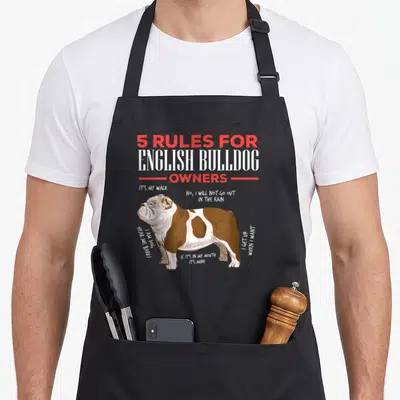Rule english chef aprons - Cartoon brown and white bulldog with humorous owner rules text in red and white — shown on a black cotton canvas apron against a white background