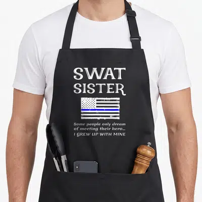 Proud swat bbq apron - SWAT SISTER text above distressed thin blue line flag with quote — shown on a black cotton canvas apron against a white background