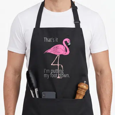 Putting pink flamingo apron - Pink flamingo cartoon standing on one leg with white punny text — shown on a black cotton canvas apron against a white background