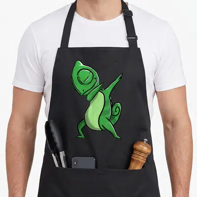 Dabbing chameleon apron - Green cartoon chameleon in a dance pose with light green belly and striped tail — shown on a black cotton canvas apron against a white background