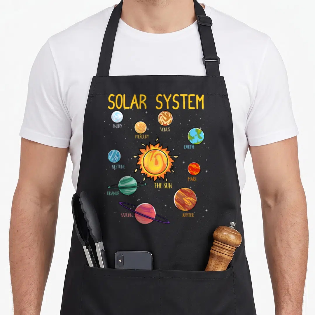 System science apron - Cartoon solar system with labeled planets Pluto Mercury Venus Earth Neptune Mars Uranus Saturn — shown on a black cotton canvas apron against a white background