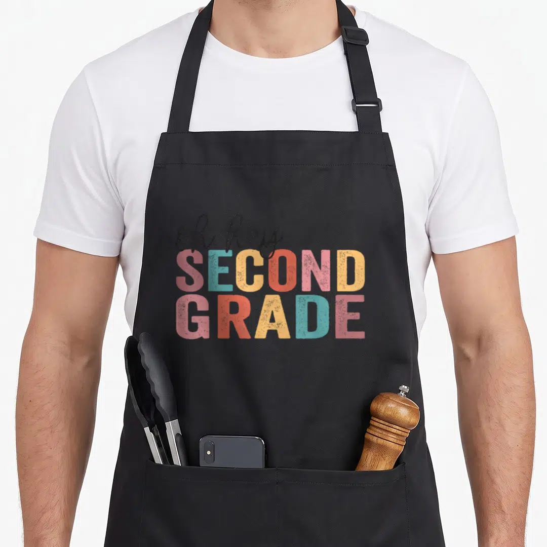 Second grade teacher apron - Stacked oh hey SECOND GRADE text in pink teal yellow and red block letters — shown on a black cotton canvas apron against a white background