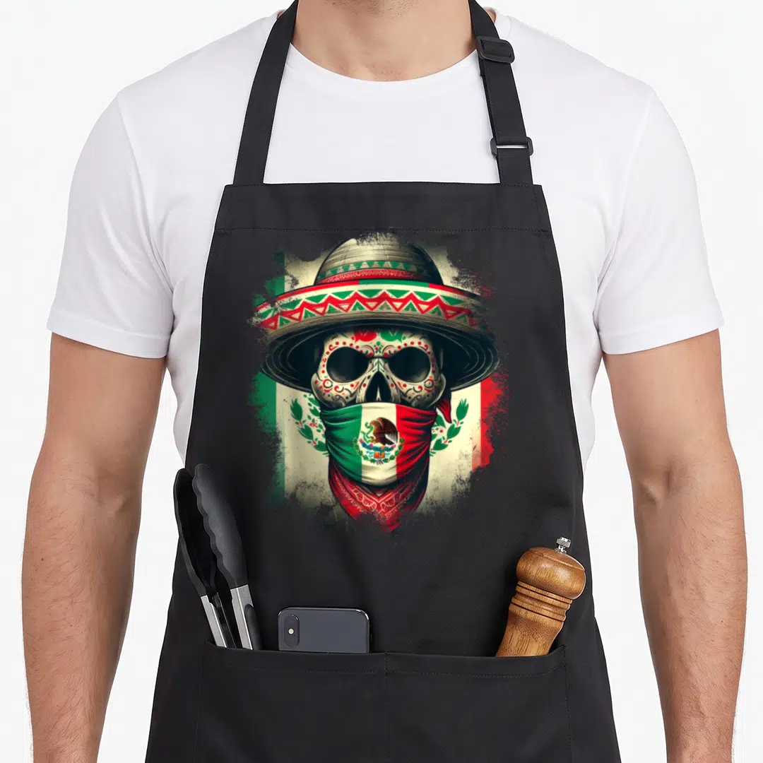 Xico mexico apron - Skull in sombrero and Mexican flag bandana with green white red brown splatter art — shown on a black cotton canvas apron against a white background
