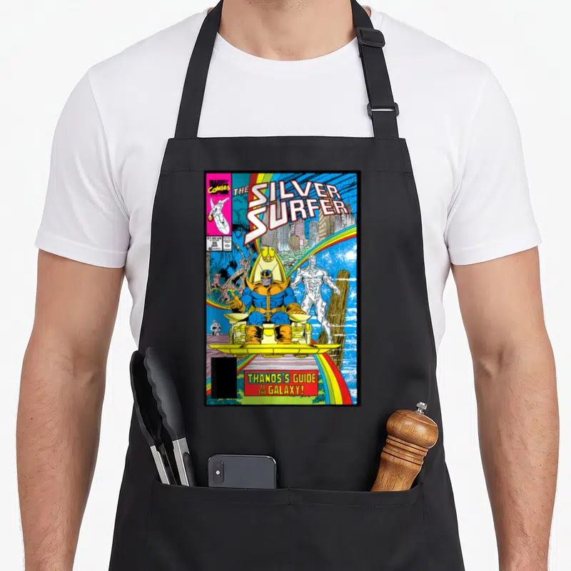 Surfer rainbow apron - Thanos on gold throne with Silver Surfer under rainbow and Marvel comic text — shown on a black cotton canvas apron against a white background