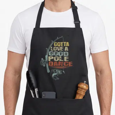 Pole fishing aprons - GOTTA LOVE A GOOD POLE DANCE text over fishing rod and bass illustration in distressed colors — shown on a black cotton canvas apron against a white background