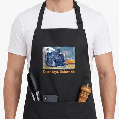Durango colorful aprons - Blue steam locomotive photo above orange Durango Colorado text on mountain background — shown on a black cotton canvas apron against a white background
