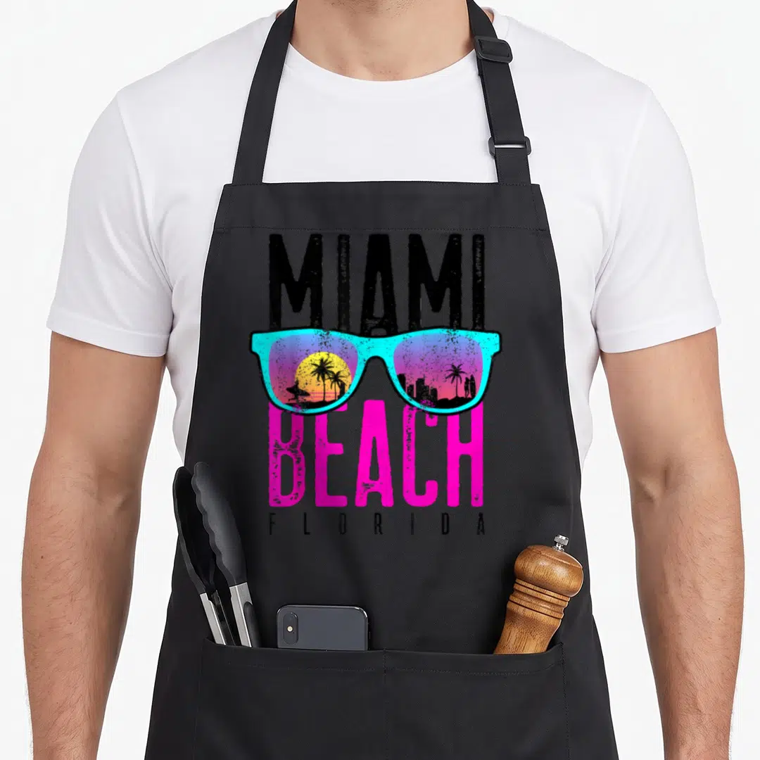 Surf florida apron - Retro cyan sunglasses with Miami Beach Florida text and silhouettes of palm trees and a surfer — shown on a black cotton canvas apron against a white background