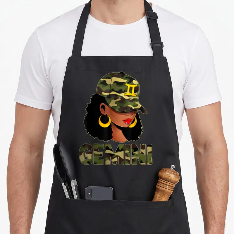 Gemini camouflage apron - Cartoon woman in camo cap and gold earrings above camo-filled GEMINI text — shown on a black cotton canvas apron against a white background
