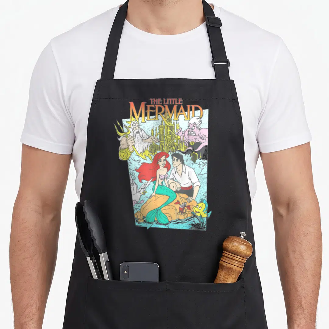 Movie mermaid apron - Vintage Little Mermaid cartoon print with Ariel Eric and castle on orange rock — shown on a black cotton canvas apron against a white background