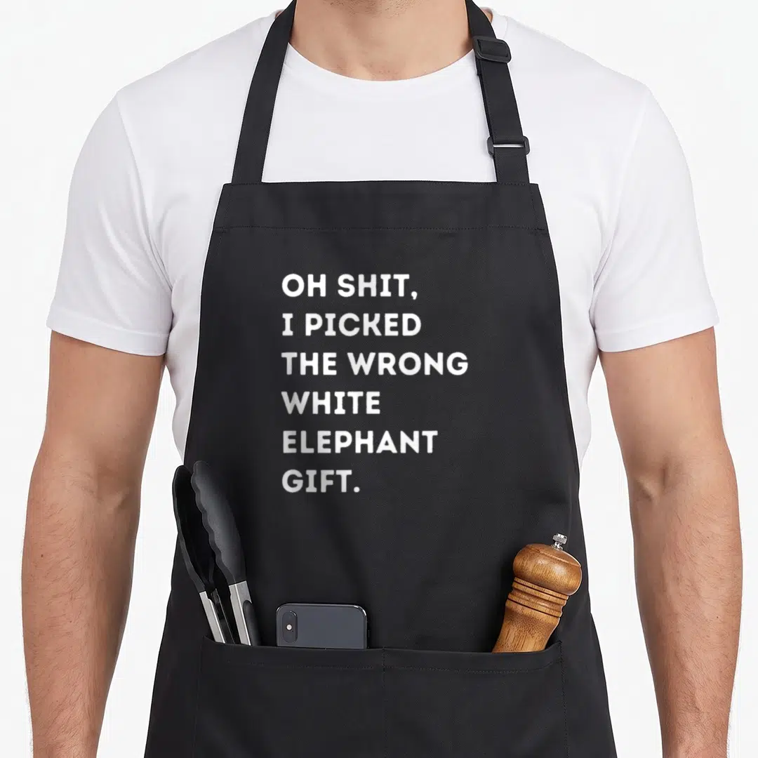 Funny elephant print apron - White text reading OH SHIT I PICKED THE WRONG WHITE ELEPHANT GIFT stacked in six lines — shown on a black cotton canvas apron against a white background