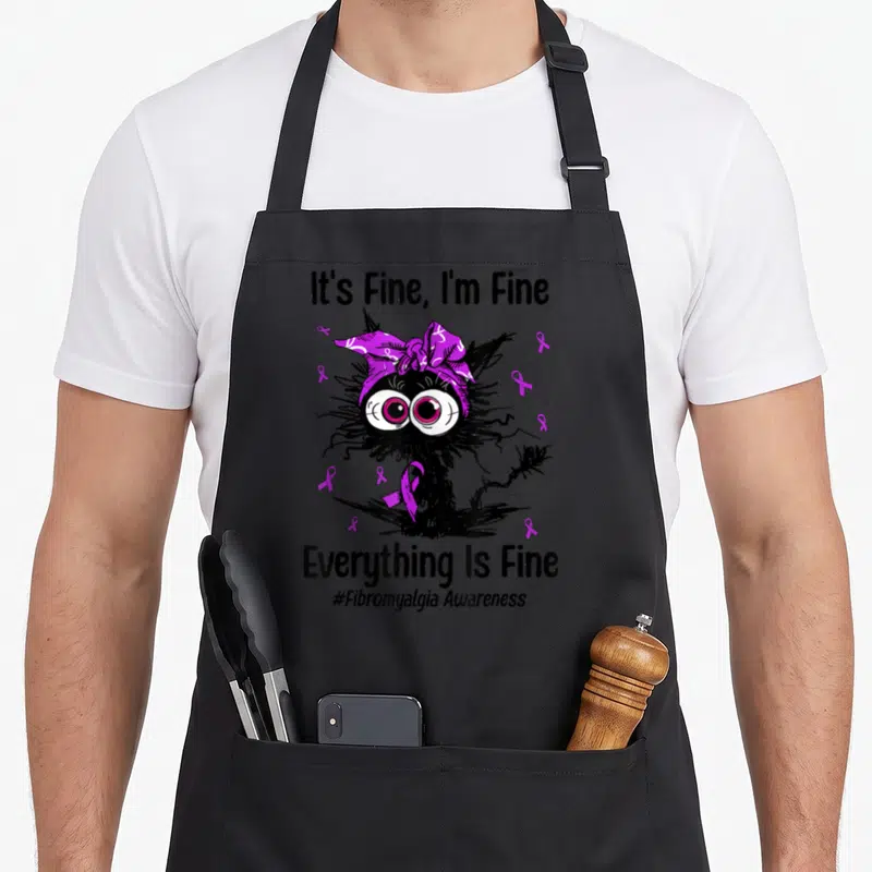 Fibromyalgia cat apron - Black monster with purple ribbons and It's Fine text — shown on a black cotton canvas apron against a white background