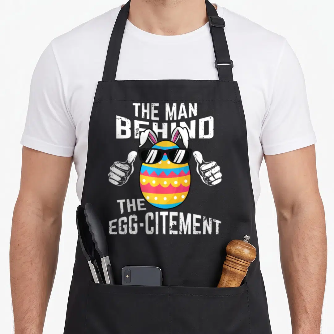 Behind easter egg apron - Cartoon Easter egg with sunglasses, bunny ears, and thumbs up flanked by white text — shown on a black cotton canvas apron against a white background