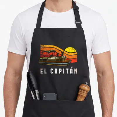 Pontoon el capitan apron - Retro boat with cheering silhouettes against orange and yellow sunset stripes with El — shown on a black cotton canvas apron against a white background
