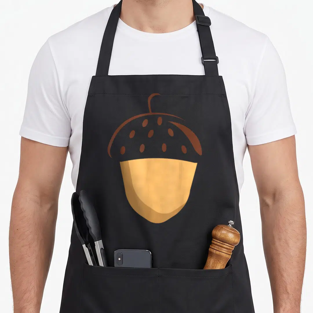 Acorn easy apron - Minimalist brown acorn with tan nut and dotted cap centered on black fabric — shown on a black cotton canvas apron against a white background