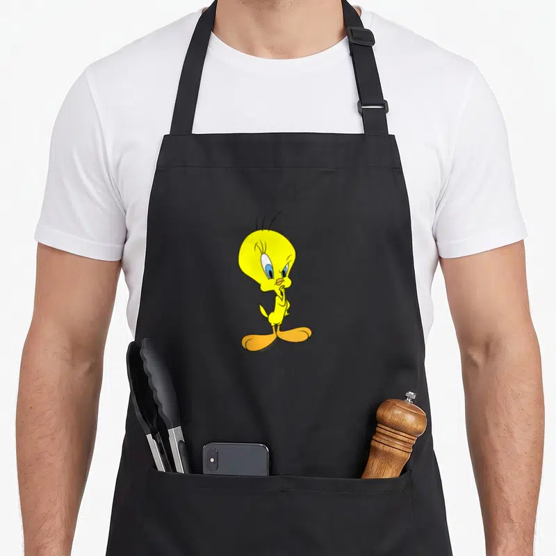 Funny tweety bird apron - Yellow cartoon bird with orange feet standing centrally with a finger to its beak — shown on a black cotton canvas apron against a white background