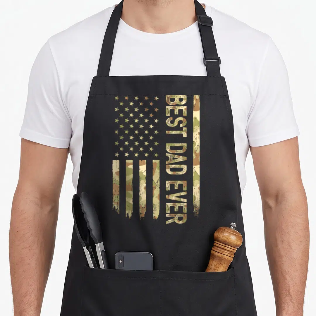 Flag father camo apron - Distressed US flag filled with olive and brown camo, vertical BEST DAD EVER text — shown on a black cotton canvas apron against a white background