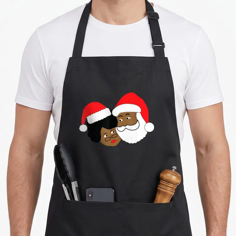 Loving mrs apron - Cartoon Santa and Mrs. Claus heads leaning together wearing red hats with brown skin tones — shown on a black cotton canvas apron against a white background
