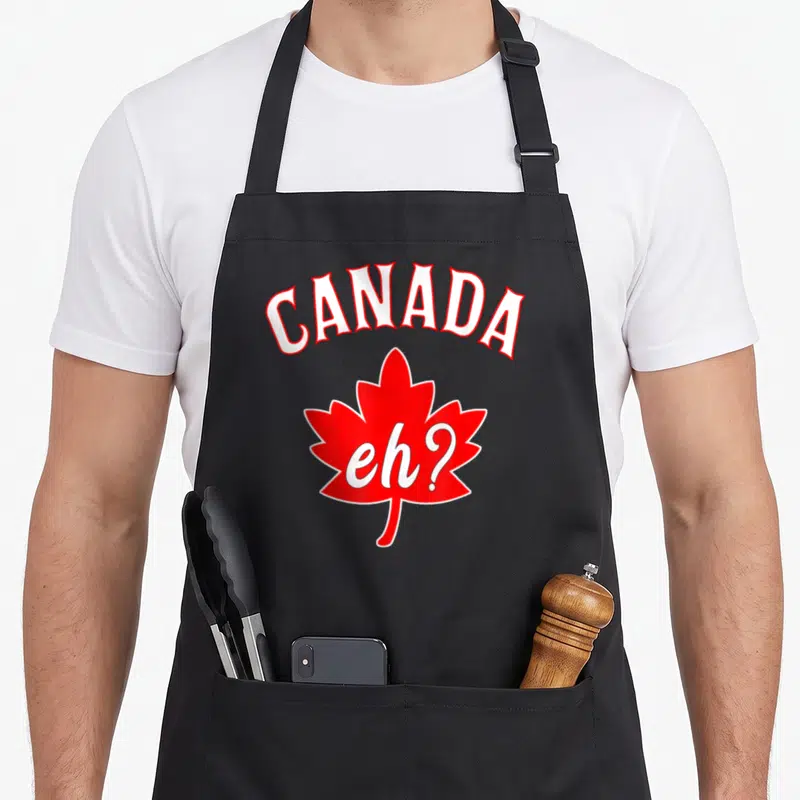 Canadian maple canada aprons - Red maple leaf with CANADA arched above and eh? printed in white script inside the leaf — shown on a black cotton canvas apron against a white background