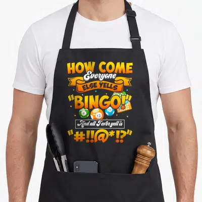 Else bingo apron - Cartoon text reading How Come Everyone Else Yells Bingo with orange white blue and green balls — shown on a black cotton canvas apron against a white background