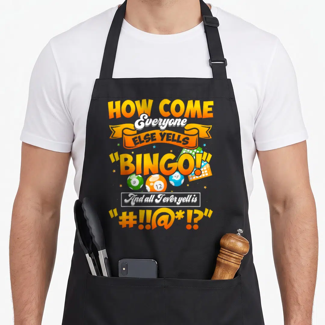 Else bingo apron - Cartoon text reading How Come Everyone Else Yells Bingo with orange white blue and green balls — shown on a black cotton canvas apron against a white background